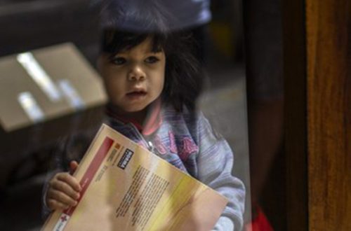 Una niña de tres años sostiene un libro infantil mientras su padre recibe una donación de comida de una ONG en su casa en Barcelona, España. Foto Ap