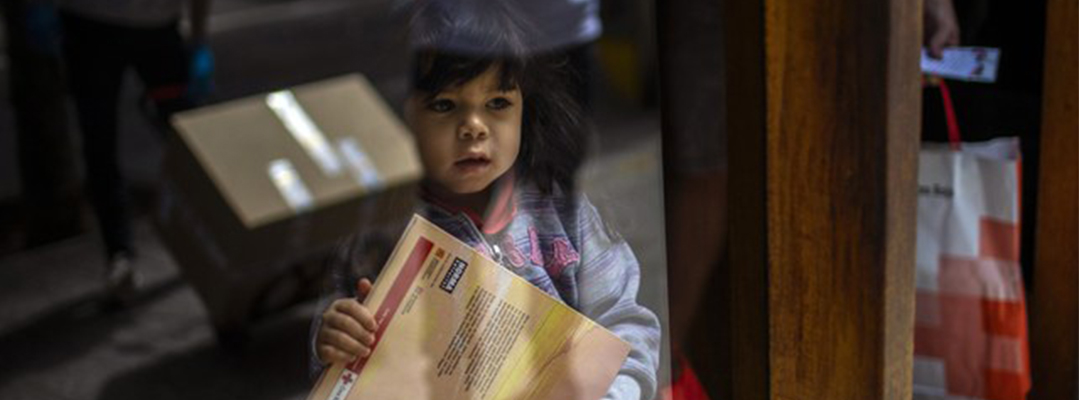 Una niña de tres años sostiene un libro infantil mientras su padre recibe una donación de comida de una ONG en su casa en Barcelona, España. Foto Ap