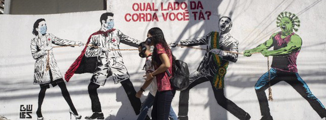 Jóvenes caminan en calles de Sao Paulo, Brasil, frente a un mural que representa la lucha de médicos contra el Covid-19 y Jair Bolsonaro. Foto Ap