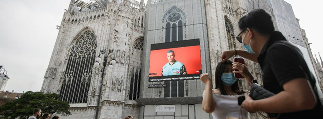 Transeúntes pasan debajo de una pantalla instalada en la Catedral del Duomo, ubicada en Milán, muestra a una modelo de Moschino, durante la Semana de la Moda Digital de Milán, Italia, el 14 de julio de 2020. Foto Ap