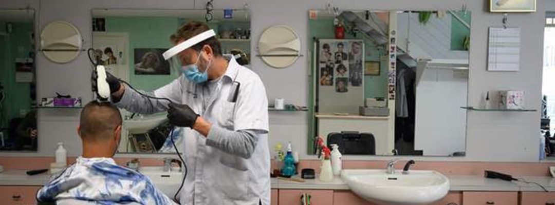 Un estilista rapa a un cliente, utilizando una máscara protectora y guantes en Suiza, donde se han relajado las restricciones por el coronavirus. Foto Afp